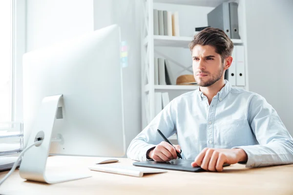 Geconcentreerde jonge man-ontwerper die werkt met computer en grafisch tablet — Stockfoto