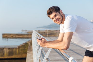 Cep telefonu ayakta ahşap balkon kullanarak gülümseyen genç sporcu