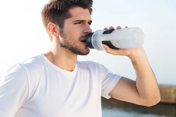 Спортсмен в белой рубашке пьет воду на открытом воздухе — стоковое фото