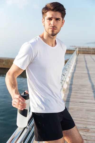 Sportsman debout sur la jetée et tenant une bouteille d'eau — Photo