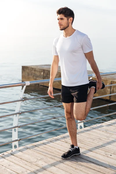 Sportowca ćwiczeń i rozciąganie nogi na molo, w pobliżu morza — Zdjęcie stockowe