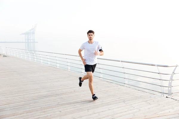 Уверенный молодой человек спортсмен, бегущий на пирсе — стоковое фото
