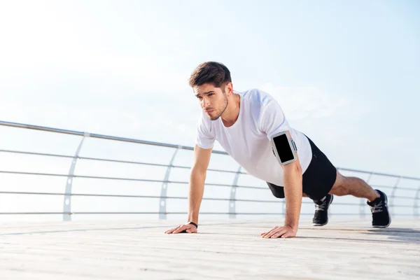 Красивый молодой спортсмен делает упражнения на доске на пирсе на открытом воздухе — стоковое фото