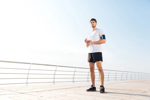 Pensativo jovem e bonito desportista em pé no cais da praia — Fotografia de Stock