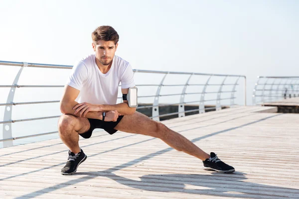 Young sportsman stretching legs during workout on pier — Stock Photo, Image