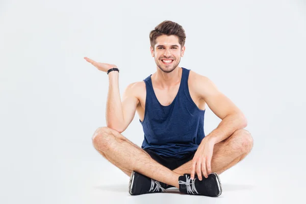 Glücklicher junger athletischer Mann sitzt und Kopierraum auf der Handfläche hält — Stockfoto