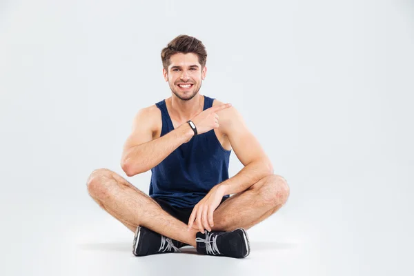 Homme de fitness souriant assis avec les jambes croisées et pointant du doigt — Photo