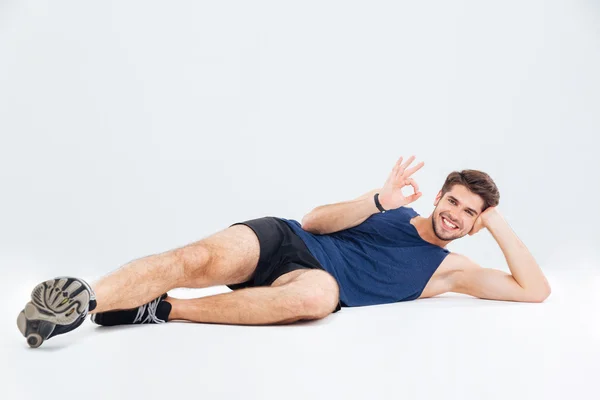 Relajado joven atlético mintiendo y mostrando signo de ok — Foto de Stock