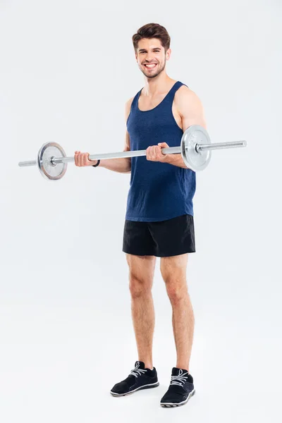 Fröhlicher junger Mann im Stehen und Training mit der Langhantel — Stockfoto