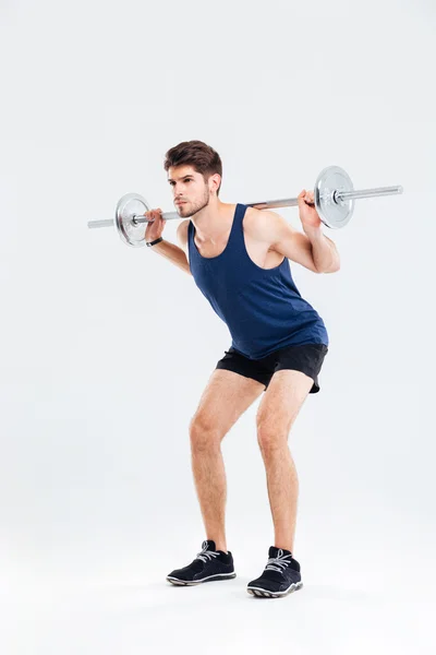 Attractive jovem desportista segurando barbell e fazendo agachamentos — Fotografia de Stock