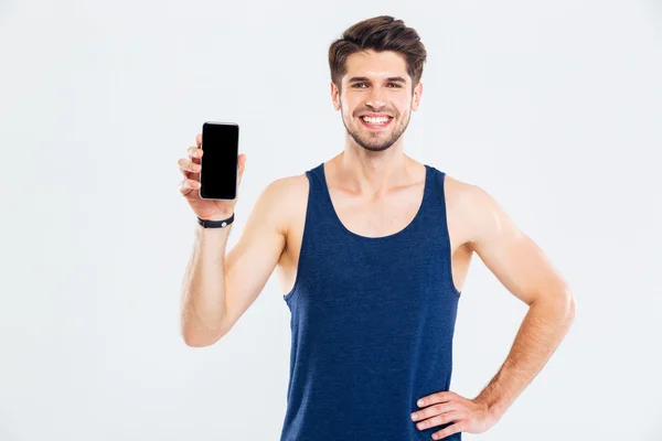 Joven deportista alegre de pie y sosteniendo la pantalla en blanco del teléfono móvil — Foto de Stock