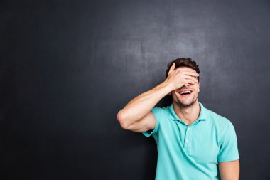 Gülümseyen yakışıklı adam elleriyle yüzünü kaplayan