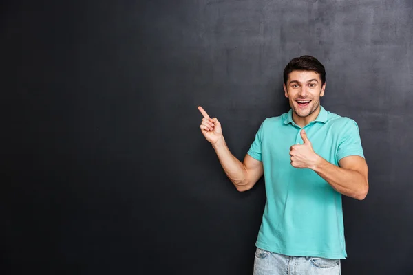 Jovem feliz apontando para longe e mostrando os polegares para cima — Fotografia de Stock