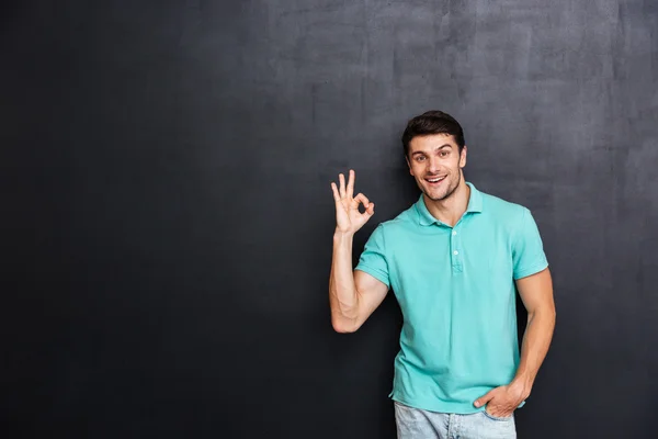 Sorrindo jovem de pé e mostrando sinal ok — Fotografia de Stock