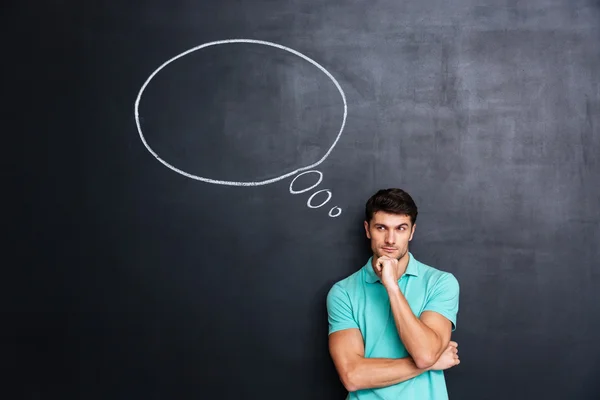 Thoughtful young man over blackboard background with blank speech bubble — Stock Photo, Image