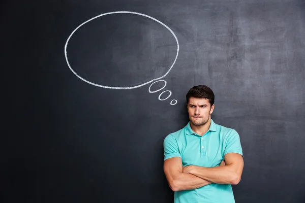 Sad frowning young man standing over chalkboard background — Stock Photo, Image