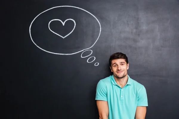 Shy cute young man thinking about love over blackboard background — Stock Photo, Image