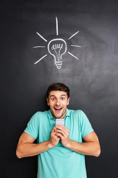 Cheerful excited young man holding smartphone and having an idea — Stock Photo, Image