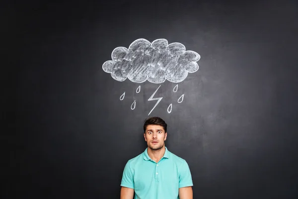 Zaskoczony zdziwiony człowiek stojący pod Raincloud wyciągnąć na tle tablicy — Zdjęcie stockowe