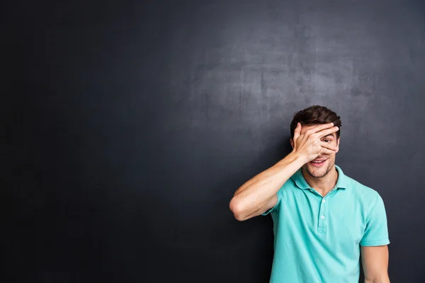 Casual man covering his eyes with fingers over black background — Stock Photo, Image