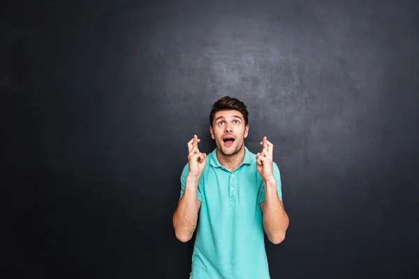 Handsome young man with his fingers crossed isolated over black — Stock Photo, Image