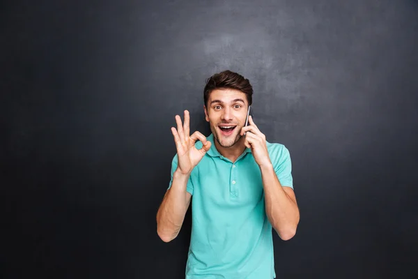 Cheerful man talking on cell phone and showing ok sign — Stock Photo, Image