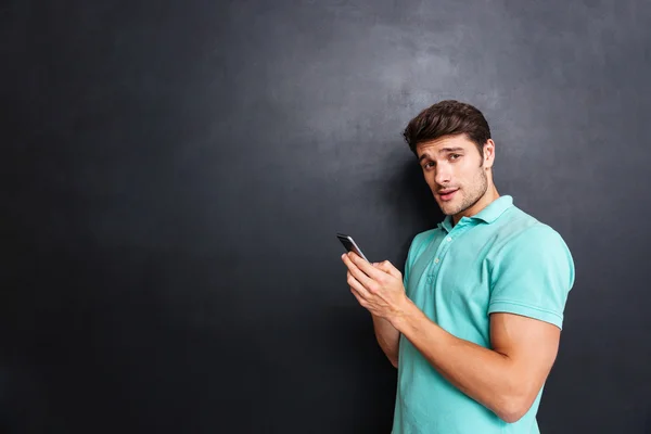 Zelfverzekerde knappe jonge man staan en het gebruik van smartphone — Stockfoto