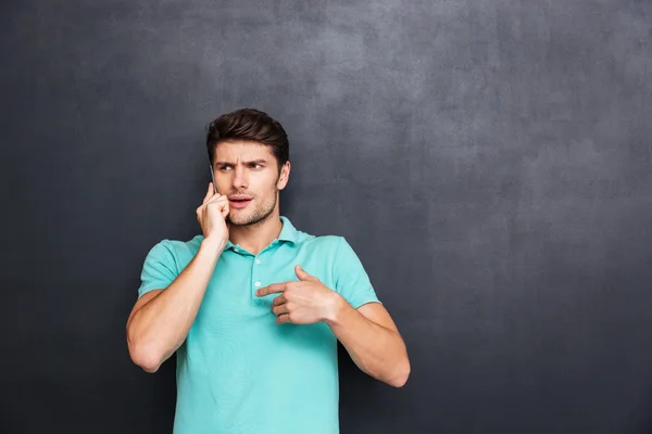 Confused handsome young man standing and talking on cell phone — Stock Photo, Image