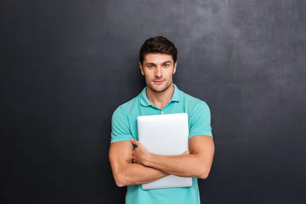 Serious confident young man standing and holding laptop — Stock Photo, Image