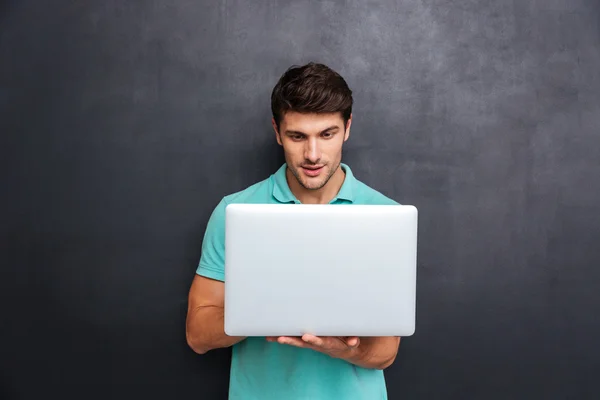 Concentrato bello giovane uomo in piedi e utilizzando il computer portatile — Foto Stock