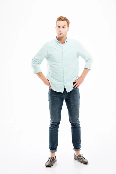 Serious suspicious young man standing with hands on hips — Stock Photo, Image