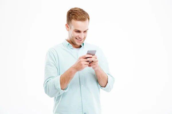 Счастливый привлекательный молодой бизнесмен, использующий смартфон и улыбающийся — стоковое фото