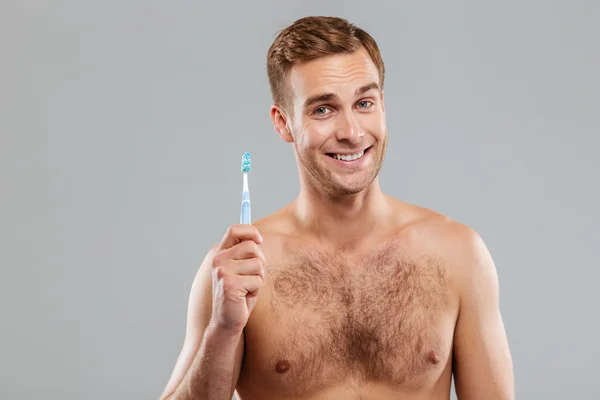 Homem feliz segurando escova de dentes no fundo cinza — Fotografia de Stock