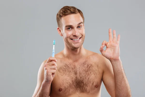 Diş fırçası basılı tutup ok işaret gösteren mutlu genç adam — Stok fotoğraf