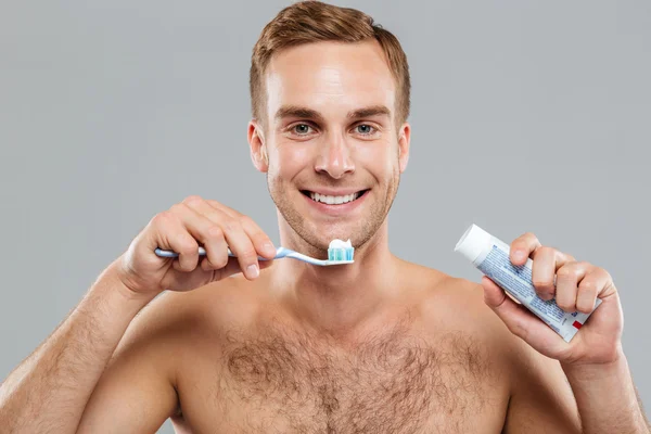 Jovem nu feliz limpando dentes com escova de dentes e pasta de dentes — Fotografia de Stock