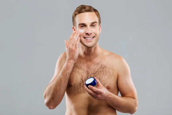 Sonriente hombre poniendo crema loción en la cara —  Fotos de Stock