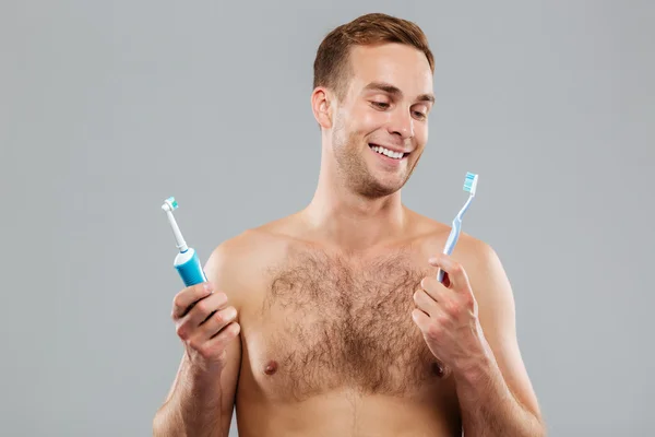 Hombre eligiendo cepillo de dientes sobre fondo gris — Foto de Stock