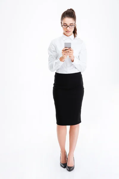 Bella giovane donna d'affari in occhiali in piedi e utilizzando smartphone — Foto Stock