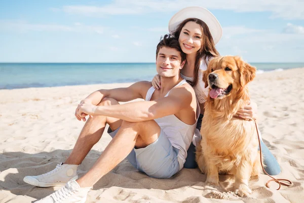 Casal apaixonado brincando com seu cão na praia — Fotografia de Stock