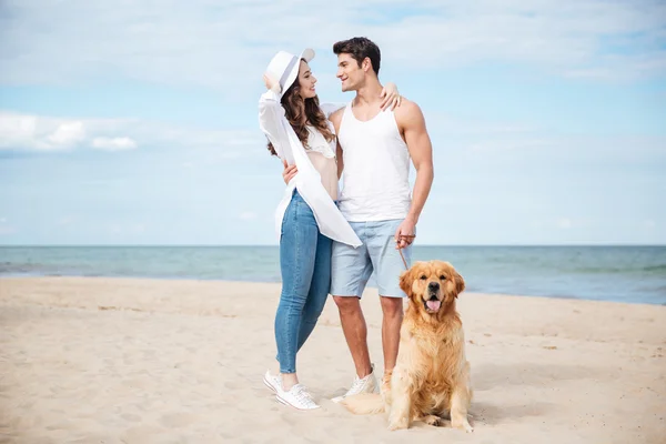 Ευτυχισμένο ζευγάρι αγκαλιάζει ενώ το περπάτημα με το σκύλο στην παραλία — Φωτογραφία Αρχείου