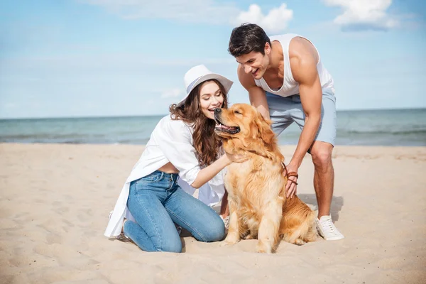 Jovem casal apaixonado sentado na praia com o cão — Fotografia de Stock