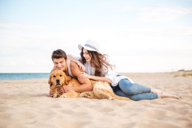 Genç teen çift sahilde oturan bir köpekle