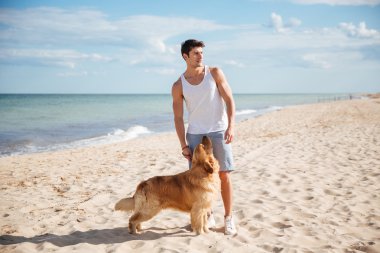 Çekici bir genç adam köpeğiyle sahilde duran