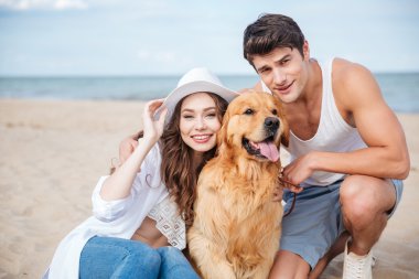 Sahilde oturmuş bir köpekle genç çekici çift