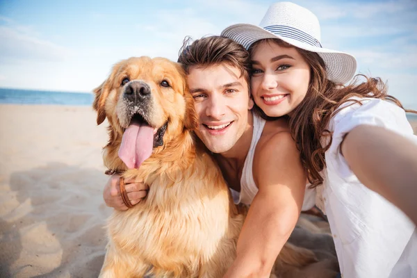 Счастливая пара обнимает свою собаку и улыбается на пляже — стоковое фото