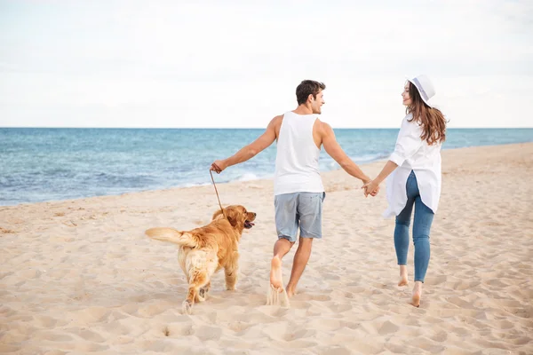 Lyckliga glada unga paret körs på stranden med sin hund — Stockfoto