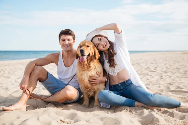 Jovem casal feliz com cão sentado na praia — Fotografia de Stock