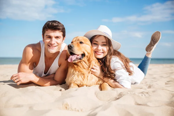 Feliz jovem casal abraçando com cão na praia — Fotografia de Stock