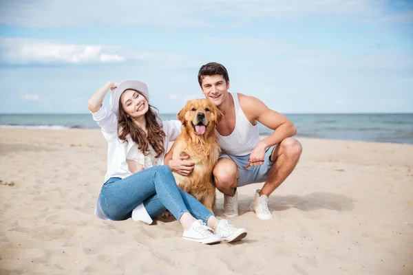 Jovem casal amoroso brincando com seu cão à beira-mar — Fotografia de Stock