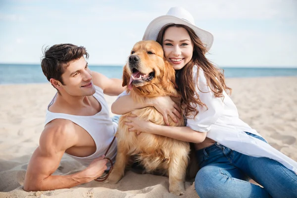 Lachende paar verliefd zittend op het strand met hond — Stockfoto